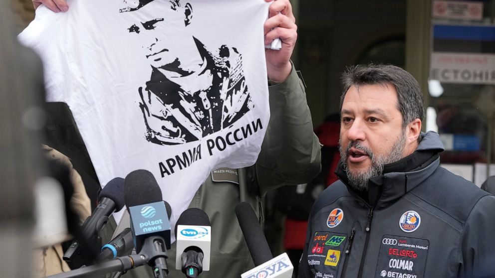 The Mayor of Przemysl, Wojciech Bakun, left, holds up a t-shirt with the likeness of Russian President Vladimir Putin and the words "The Russian Army" as Italy's League Party leader, Matteo Salvini, right, speaks with journalists outside the train st