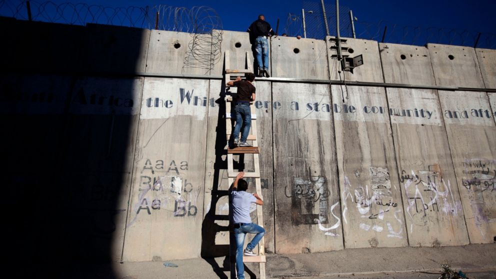 FILE - Palestinians use a ladder to climb over the separation barrier with Israel on their way to pray at the al-Aqsa Mosque in Jerusalem during the Muslim holy month of Ramadan, in Al-Ram, north of Jerusalem, July 11, 2014. Israel on Monday, Jan. 31