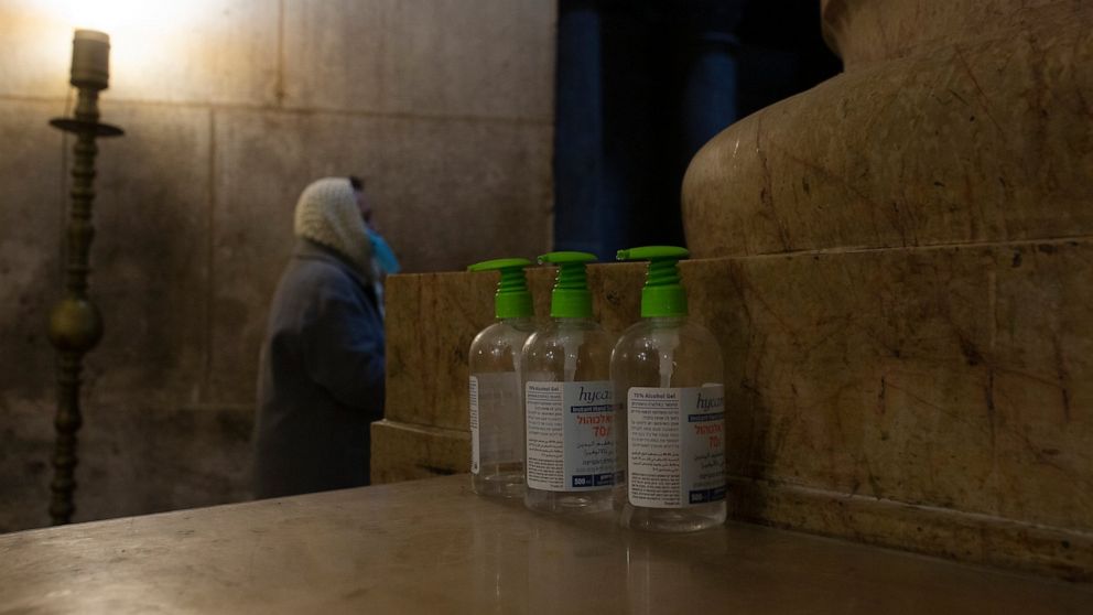 A woman attends mass next to three bottles of hand sanitizer available for worshippers at the Church of the Holy Sepulchre, where Jesus Christ is believed to be buried, during a third lockdown to curb the spread of the coronavirus, in the Old City of