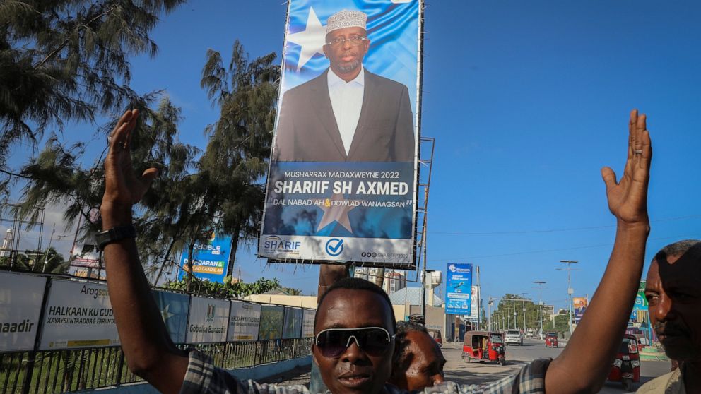 Supporters raise their hands near a campaign poster for former president and presidential candidate Sharif Sheikh Ahmed, on a street in Mogadishu, Somalia Tuesday, May 10, 2022. Somalia is set to hold its long-delayed presidential vote on Sunday, end