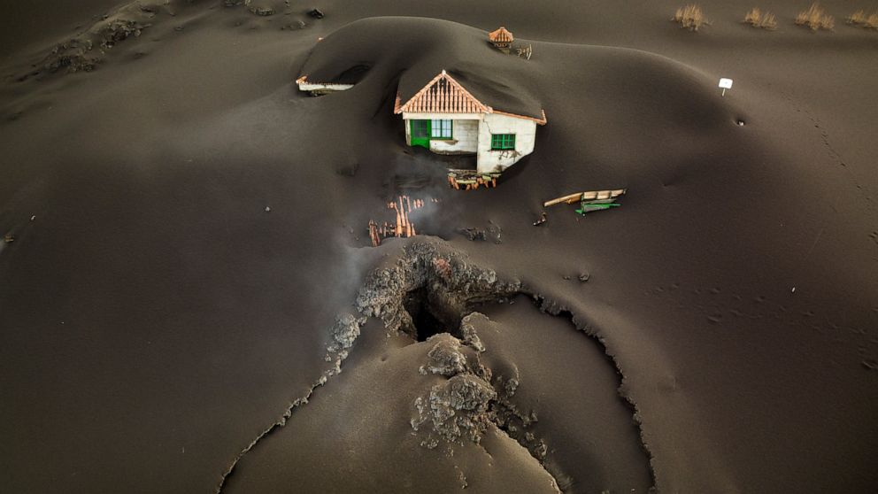 A fissure is seen next to a house covered with ash on the Canary island of La Palma, Spain, Wednesday, Dec.1 2021. A fissure that volcanologists believe spouted a gusher of lava left a gaping hole in front of house whose bottom floor was completely c