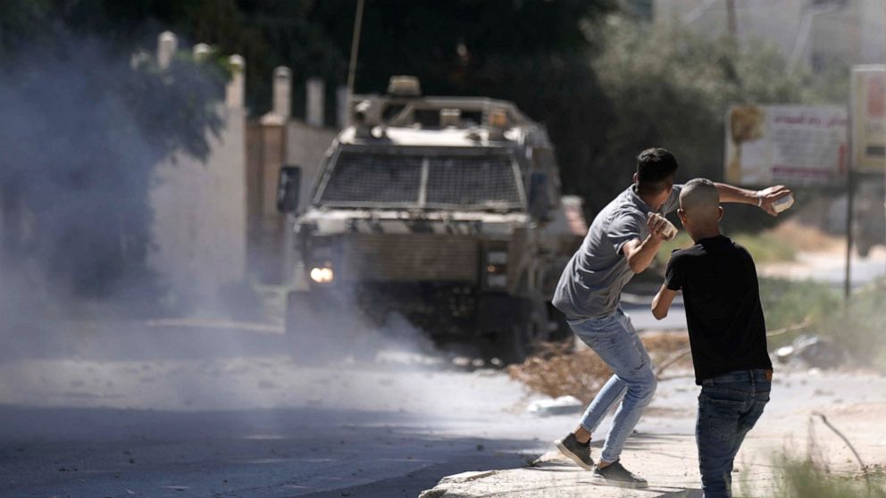 A Palestinian throws stones at an Israeli military vehicle following a deadly raid in the occupied West Bank town of Jenin, Wednesday, Sept. 28, 2022. At least four Palestinians were killed and dozens of others wounded, the Palestinian Health Ministr
