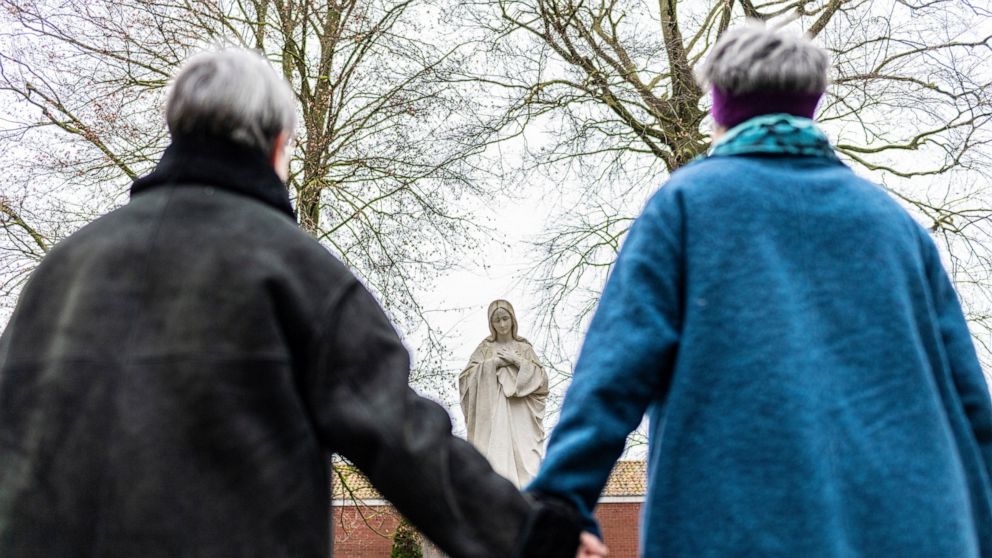 Monika Schmelter, left, and Marie Kortenbusch, right, stand hand in hand in front of a statue of Mary at a convent in Luedinghausen, Germany, Monday, Jan. 24, 2022. More than 100 employees of the Catholic Church in Germany publicly outed themselves a