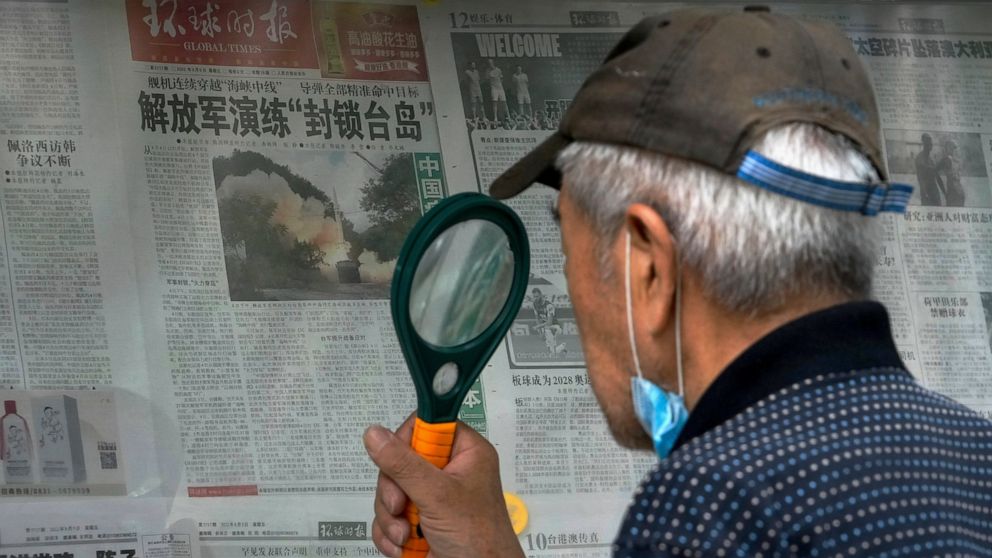 A man uses a magnifying glass to read a newspaper headline reporting on Chinese People's Liberation Army (PLA) conducting military exercises, at a stand in Beijing, Sunday, Aug. 7, 2022. U.S. Secretary of State Antony Blinken said Saturday that China