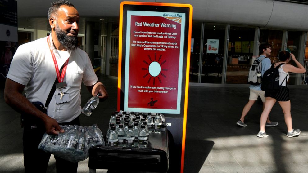 A railway worker hands out bottles of water to passengers at King's Cross railway station where there are train cancellations due to the heat in London, Tuesday, July 19, 2022. Millions of people in Britain woke from the country's warmest-ever night 