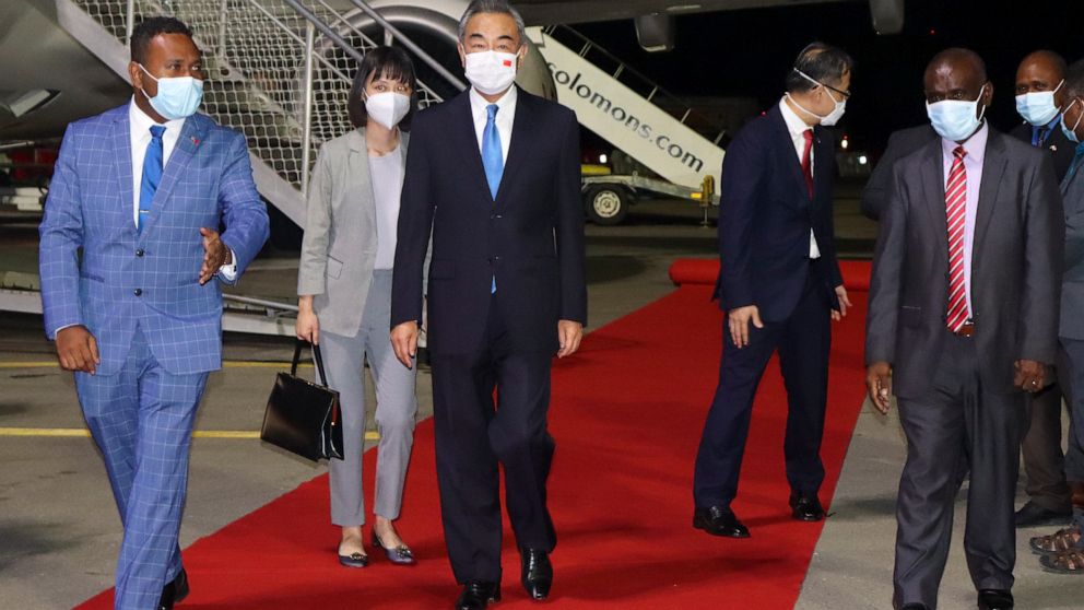 China's Foreign Minister Wang Yi, center, is escorted from his plane on his arrival in Honiara, Solomon Islands, early Thursday, May 26, 2022. Wang and a 20-strong delegation arrived in the Solomon Islands Thursday at the start of an eight-nation tou
