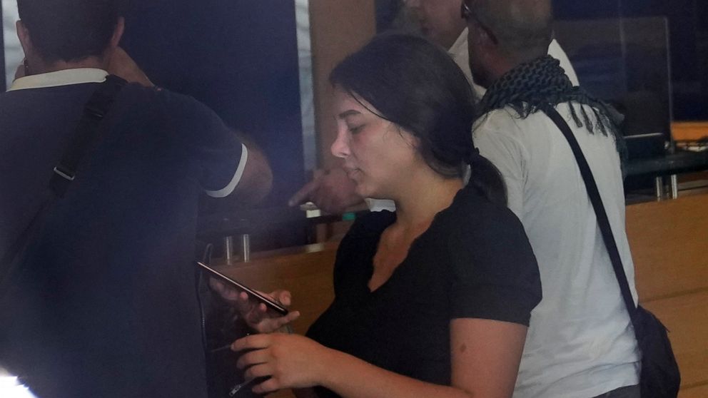 Lebanese Sali Hafez, center, accompanied by activists looks at her phone after breaking into a BLOM Bank branch brandishing what she later said was a toy pistol and taking $13,000 from her trapped savings accopunt, in Beirut, Lebanon, Wednesday, Sept