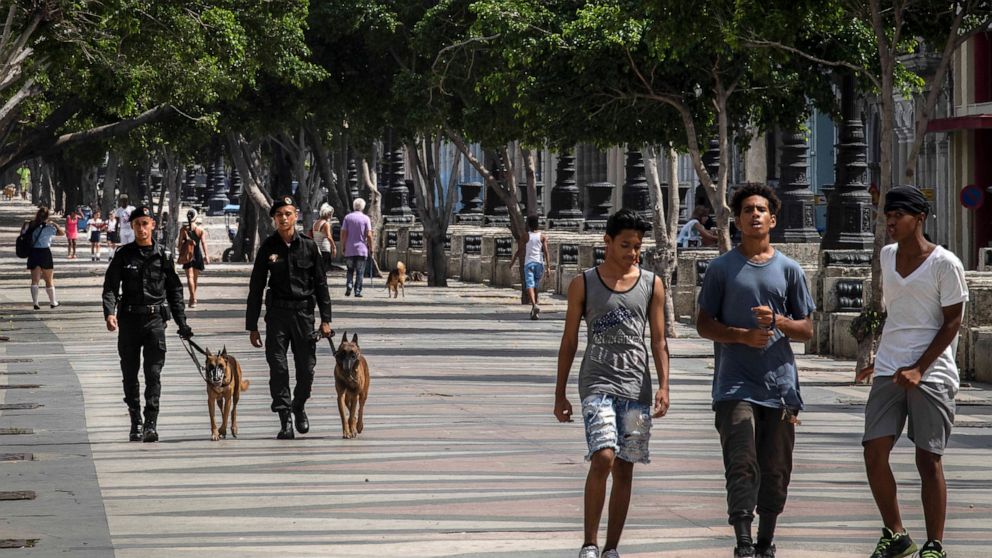 People walk at the Paseo del Prado while members of the police patrol in Havana, Cuba, Monday, July 11, 2022. A year after the largest protests in decades shook Cuba's single-party government, the economic and political factors that caused them large