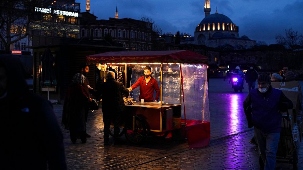 A roast chestnut seller talks to customers in Istanbul, Turkey, Thursday, Dec. 16, 2021. Turkey's Central Bank again cut a key interest rate Thursday despite soaring consumer prices that are making it difficult for people to buy food and other basic 