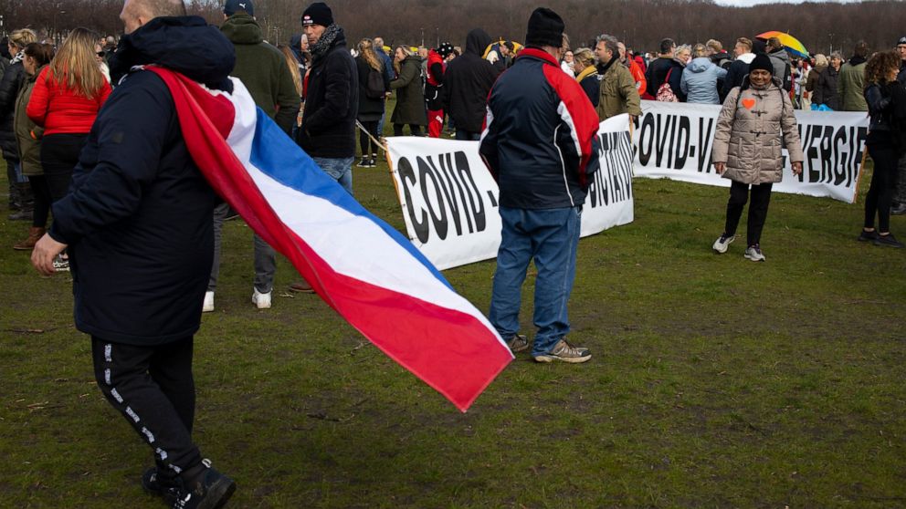 A man wearing a Dutch flag passes signs reading "COVID Rules = Dictatorship" and "COVID Vaccin = Poison" during a demonstration ahead of three days of voting starting Monday in a general election, to protest government policies including the curfew, 