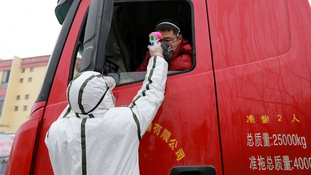 A worker in a hazardous materials suit takes the temperature of a truck driver at a checkpoint in Huaibei in central China's Anhui Province, Monday, Jan. 27, 2020. China on Monday expanded sweeping efforts to contain a viral disease by extending the 