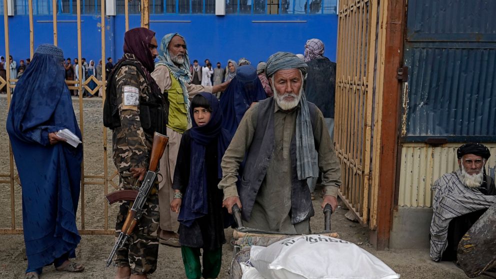 A Taliban fighter stands guard as people receive food rations distributed by a South Koren humanitarian aid group, in Kabul, Afghanistan, Tuesday, May 10, 2022. Afghanistan is expected 1.1 million children under the age of 5 will face malnutrition in