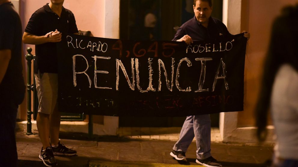 Citizens carrying a banner that reads in Spanish "Ricarod Rosello, renounce" protest near the executive mansion denouncing a wave of arrests for corruption that has shaken the country and demanding the resignation of Gov. Ricardo Rosello, in San Juan