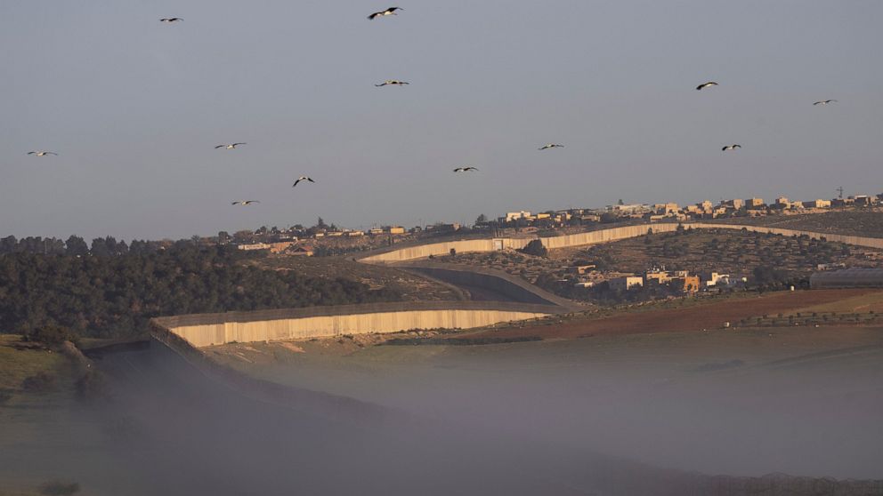 Storks fly over a section of Israel's separation barrier, between the Israeli Kibbutz Kramim and the West Bank village of Arab al Fureijat, Sunday, April 10, 2022. (AP Photo/Oded Balilty)