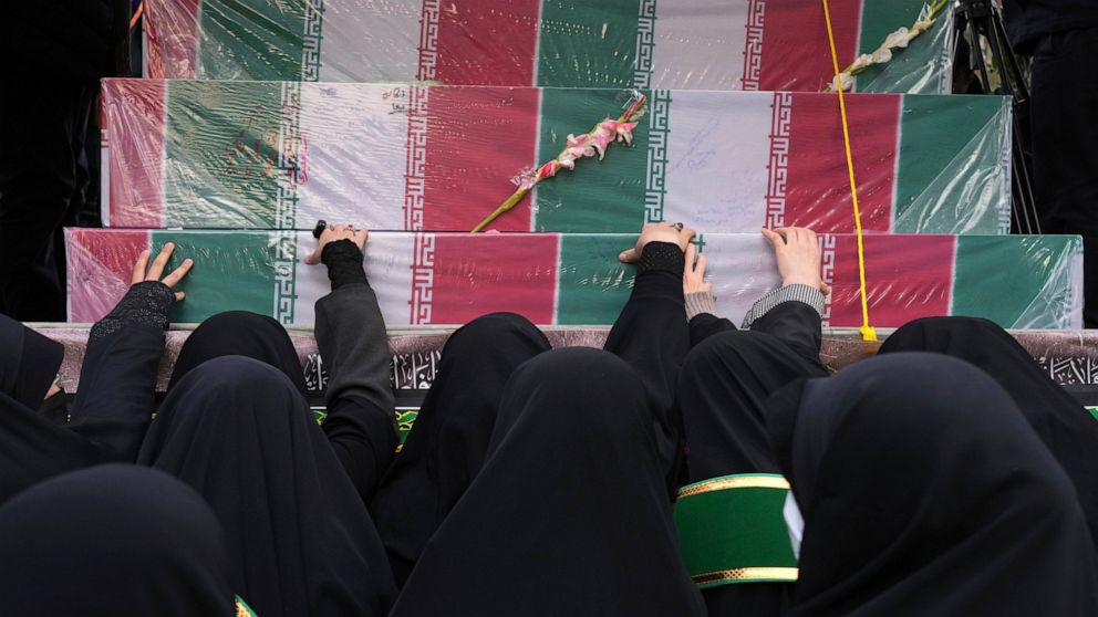 Mourners touch flag-draped coffins of unknown Iranian soldiers who were killed during the 1980-88 Iran-Iraq war, whose remains were recently recovered in the battlefields, during their funeral procession, in Tehran, Iran, Tuesday, Dec. 27, 2022. (AP 