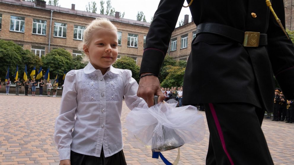 A graduate cadet holds the hand of a young schoolgirl and rings the bell on the first day of school at a cadet lyceum in Kyiv, Ukraine, Thursday, Sept. 1, 2022. (AP Photo/Efrem Lukatsky)