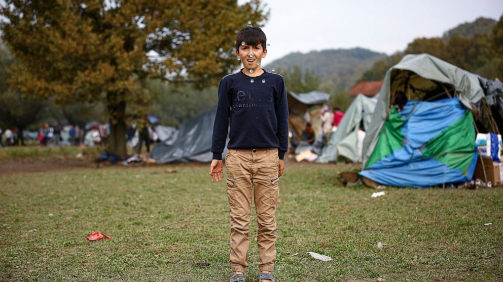 A migrant boy throws marbles in the air while posing for a photograph at a makeshift camp housing migrants mostly from Afghanistan, in Velika Kladusa, Bosnia, Tuesday, Oct. 12, 2021. Dozens of children of all ages are among migrants staying in a make