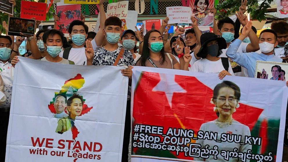 Migrant workers from Myanmar flash the three-finger protest gesture while they hold banners with images of deposed Myanmar leader Aung San Suu Kyi before participating in a march by Thai pro-democracy activists to the residence of Thai Prime Minister