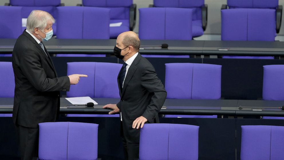 German Interior Minister Horst Seehofer, left, and German Finance Minister Olaf Scholz, right, talk as they arrive for a meeting of the German federal parliament, Bundestag, at the Reichstag building in Berlin, Germany, Wednesday, Jan. 13, 2021. One 