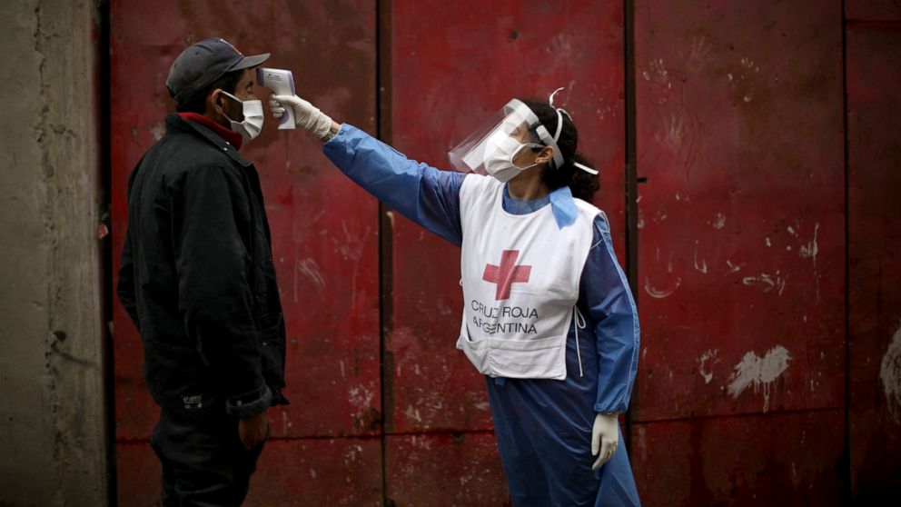 FILE - In this June 6, 2020 file photo, a Red Cross volunteer measures the temperature of man inside the Fraga slum, during a government-ordered lockdown to curb the spread of the new coronavirus, in Buenos Aires, Argentina. Argentina reached 1 milli