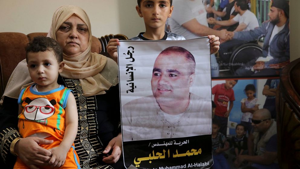 FILE - Amal el-Halabi holds her grandson Fares while her grandson Amro, 7, holds a picture of his father Mohammed el-Halabi, Gaza director of the international charity World Vision, who was convicted by an Israeli court of diverting sums to Hamas, at