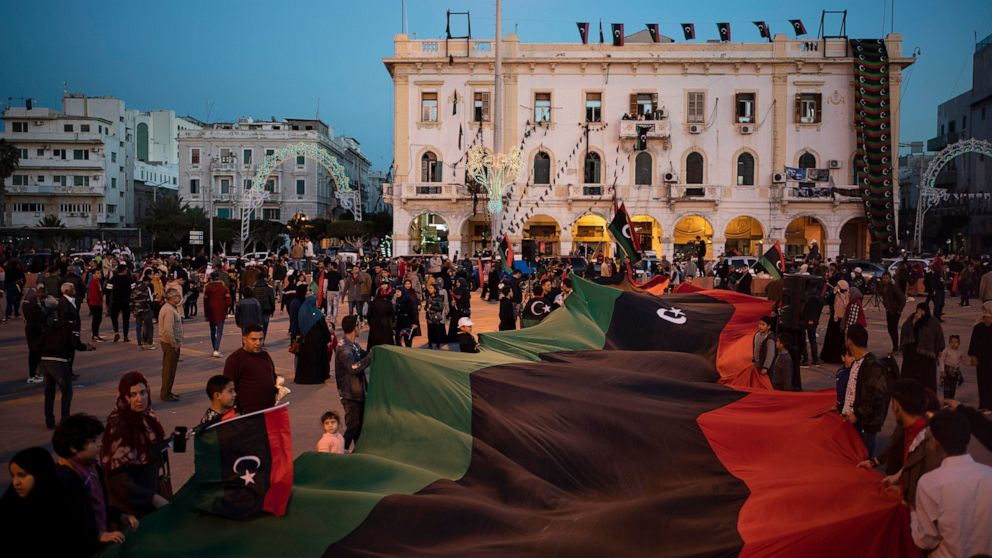 FILE - In this Feb. 25, 2020 file photo, people carry a giant Libyan flag at the Martyr square during a march commemorating the anniversary of anti-Gadhafi protests in Tripoli, Libya. A recent U.N. experts report has sketched a grim picture of confli