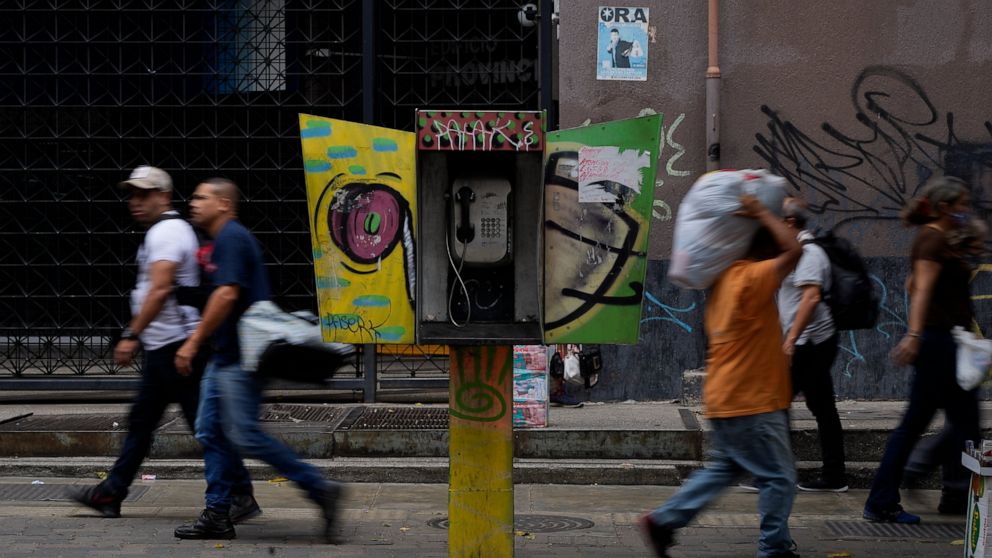 Pedestrians walk past an out of service National Telephone Company of Venezuela, CANTV, phone booth, in Caracas,Venezuela, Friday, May 13, 2022. A number of Venezuelan state-owned companies, including in the telecommunications sector, will sell up to