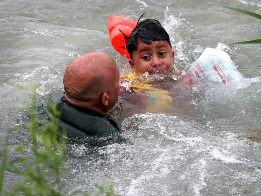 In this Friday, May 10, 2019 photo, Border Patrol Agent Brady Waikel rescues a 7-year-old boy from Honduras after he fell out of a makeshift raft and lost hold of his mother as Border Patrol agents respond to rafts crossing the Rio Grande River near