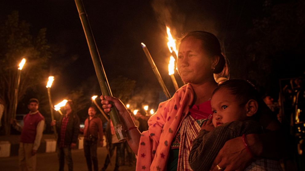 An Indian tribal woman carries a child as she participates in a torch light procession to protest against the Citizenship Amendment Bill (CAB) in Gauhati, India, Monday, Dec. 9, 2019. The bill that seeks to grant Indian citizenship to non-Muslim refu