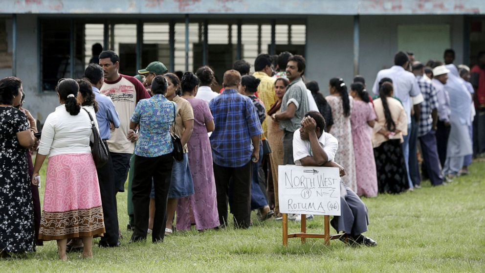 FILE - A man sits and rests while others line up at the Nadi public school in Fiji, on May 10, 2006, waiting for hours to cast their vote in the country's general election. The survey found 26% of people in the region said they had been offered bribe