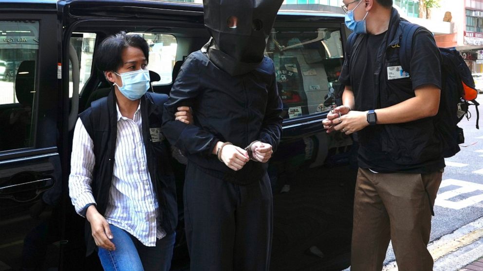 A hooded suspect is accompanied by police officers to search evidence at office in Hong Kong Thursday, July 22, 2021. Hong Kong's national security police on Thursday arrested five people from a trade union of the General Association of Hong Kong Spe