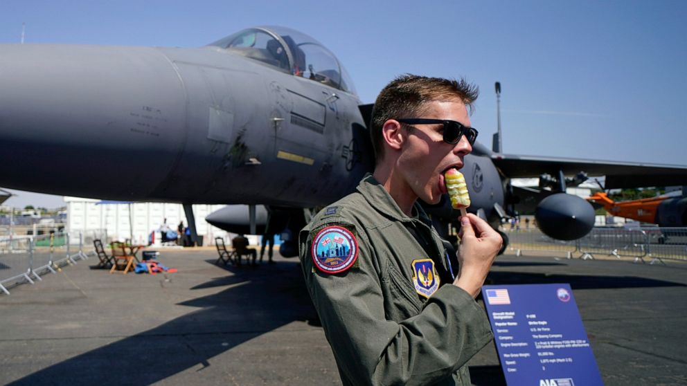 FILE - A member of the military personnel eats an ice cream as he stands past an F15E Strike Eagle fighter jet, on display at the Farnborough Air Show fair in Farnborough, England, Tuesday, July 19, 2022. The future for fighter pilots was on display 
