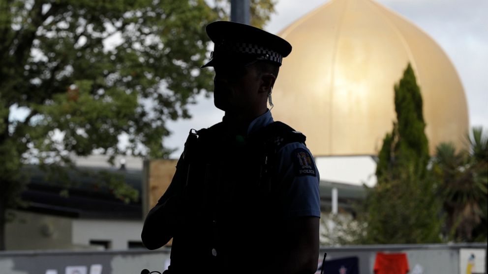 Armed police guard the Al Door mosque ahead of Friday prayers at Hagley Park in Christchurch, New Zealand, Friday, March 22, 2019. In a day without precedent in New Zealand, people across the country were planning to observe the Muslim call to prayer as the nation reflected on the moment one week ago when 50 people were slaughtered at two mosques. (AP Photo/Mark Baker)