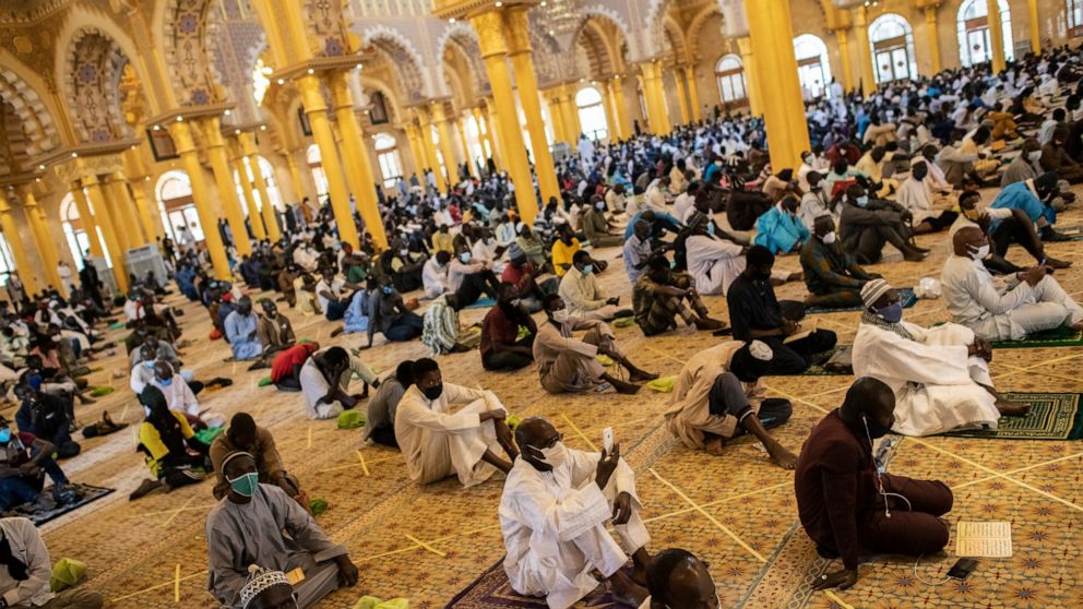 In this photo taken Friday, May 15, 2020, a follower of the Senegalese Mouride brotherhood, an order of Sufi Islam, films with his smartphone as he and others practice social distancing as they attend Muslim Friday prayers at West Africa's largest mo