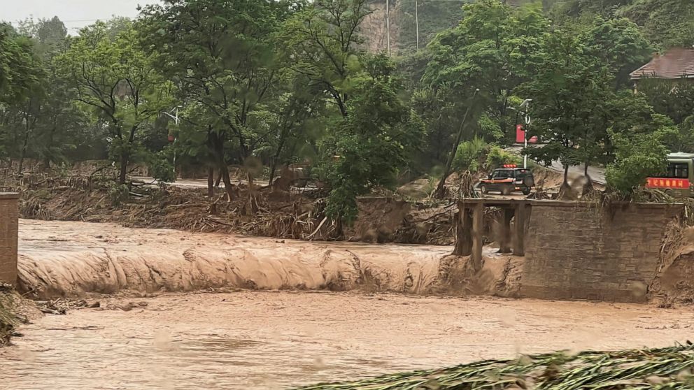A vehicle is seen near a part of a bridge that was washed away by flood waters along a river in Qingyang in northwest China's Gansu province Saturday, July 16, 2022. Flash floods in southwest and northwest China have left at least a dozen dead and pu