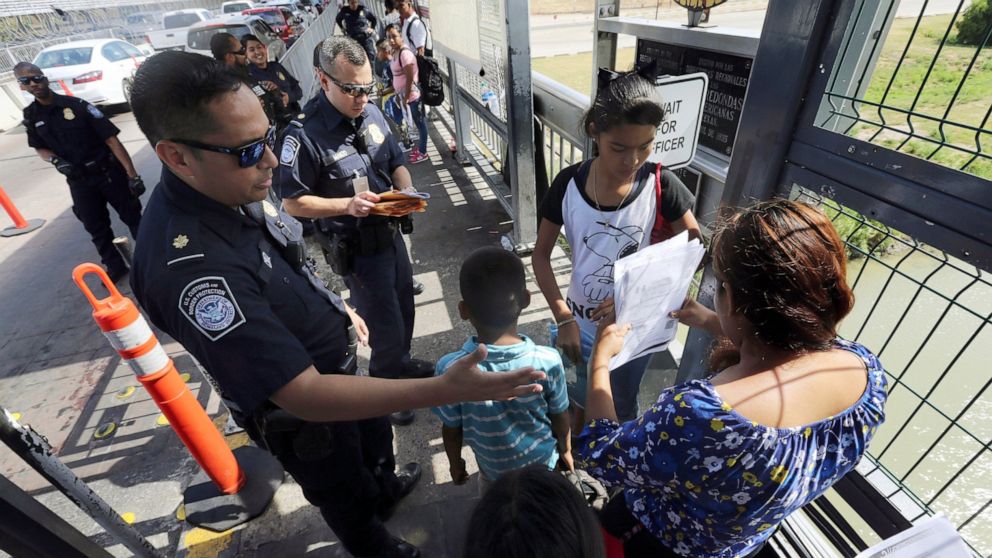 FILE - In this July 17, 2019, file photo, a United States Customs and Border Protection Officer checks the documents of migrants before being taken to apply for asylum in the United States, on International Bridge 1 in Nuevo Laredo, Mexico. A federal