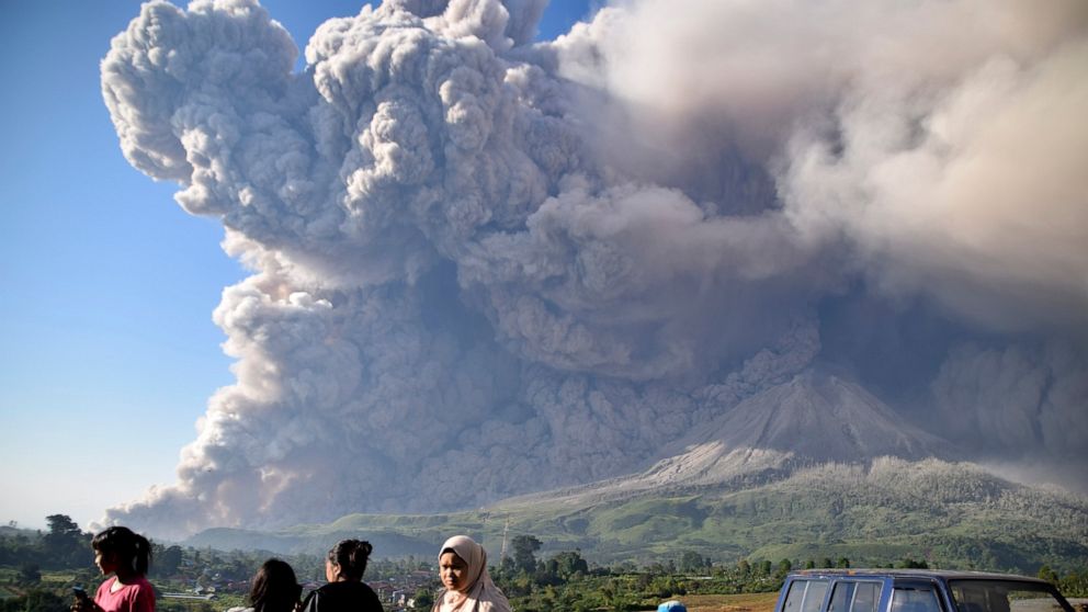 People watch as Mount Sinabung spews volcanic material during an eruption in Karo, North Sumatra, Indonesia, Tuesday, March 2, 2021. The 2,600-metre (8,530-feet) volcano erupted Tuesday, sending volcanic materials a few thousand meters into the sky a