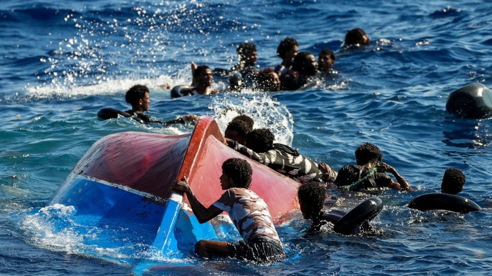 FILE - Migrants swim next to their overturned wooden boat during a rescue operation by Spanish NGO Open Arms at south of the Italian Lampedusa island at the Mediterranean sea, Aug. 11, 2022. The back-to-back shipwrecks of migrant boats off Greece tha