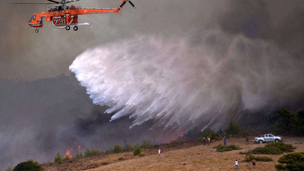 An helicopter drops water over a fire in Siderina village helicopter about 55 kilometers (34 miles) south of Athens, Greece, Monday, Aug. 16, 2021. Greek authorities have deployed dozens of firefighters, as well as six water-dropping planes and four 