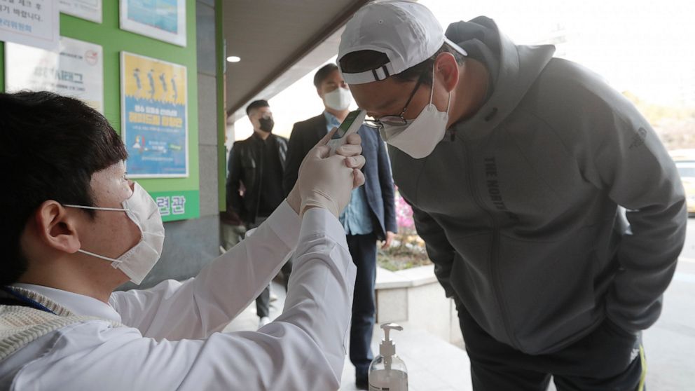A man wearing a face mask to help protect against the spread of the new coronavirus has his temperature checked upon his arrival to cast his vote for the parliamentary election at a polling station in Seoul, South Korea, Wednesday, April 15, 2020. So