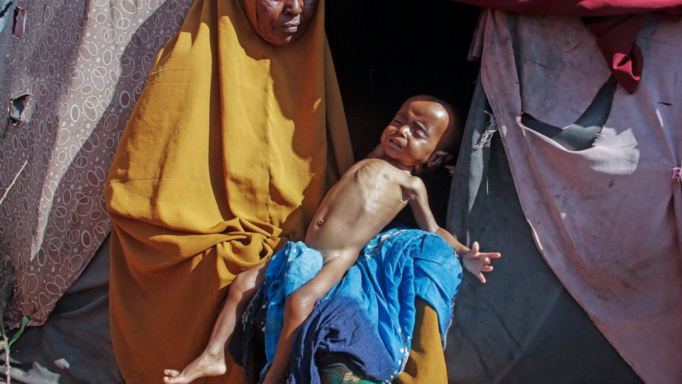 Boolo Aadan, 63, who fled drought-stricken areas, holds her 9 month old grandchild outside the tent where they now live at a makeshift camp on the outskirts of the capital Mogadishu, Somalia Friday, Feb. 4, 2022. Thousands of desperate families have 