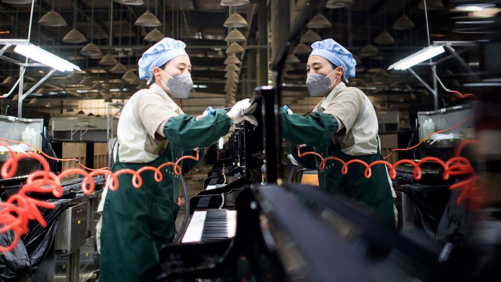 In this photo released by Xinhua News Agency, a worker cleans a piano at a production factory of Parsons Music Corporation in Yichang in central China's Hubei Province, Nov. 23, 2021. China's manufacturing activity rebounded in November as orders imp