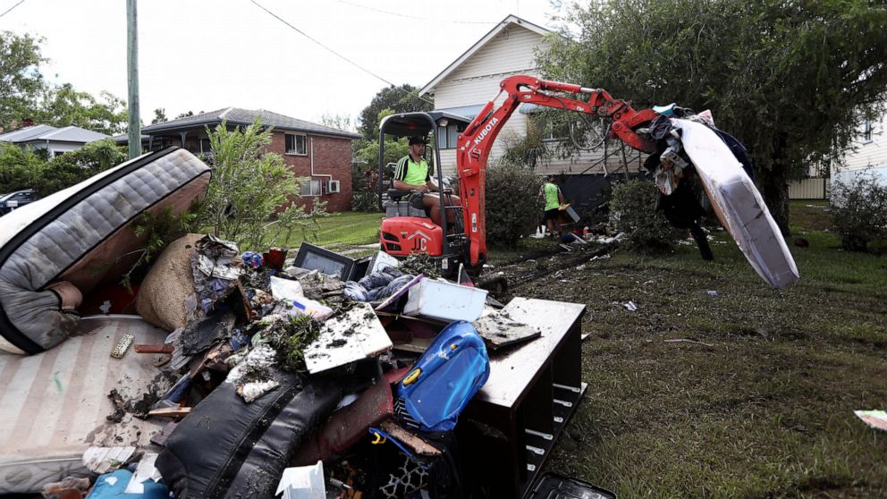 A man uses an excavator to stack debris damaged by flood water in Lismore, Australia, Wednesday, March 2, 2022. Floodwaters are moving south into New South Wales from Queensland state in the worst disaster in the region since what was described as a 