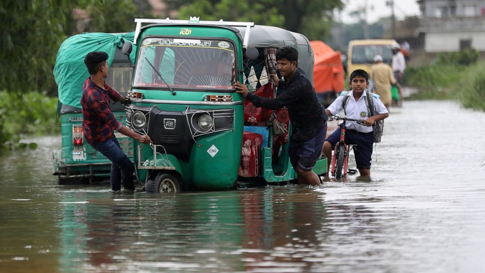People push an auto rickshaw through a flooded road as a school boy rides his bicycle behind in Bagha area in Sylhet, Bangladesh, Monday, May 23, 2022. Pre-monsoon deluges have flooded parts of India and Bangladesh, killing at least 24 people in rece