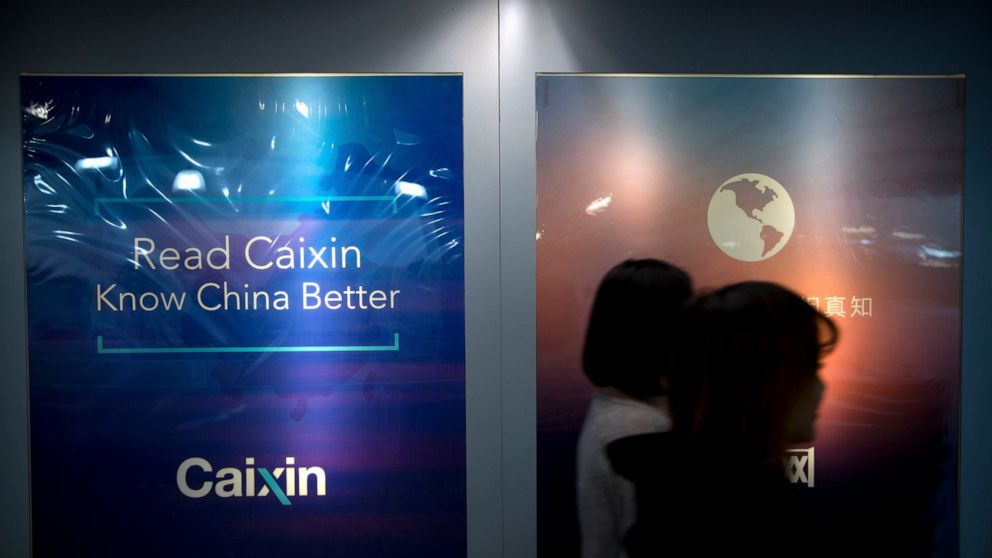 FILE - In this Jan. 18, 2018, file photo, staffers walk past a billboard reading "Read Caixin - Know China Better" at the Caixin Media offices in Beijing. China has removed Caixin Media, one of the country’s most liberal business news sites, from a l
