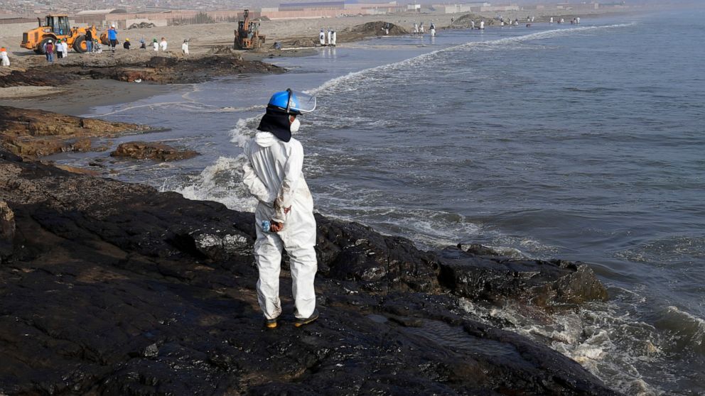 A workers stand on a rock covered with oil as other help with the clean up at Cavero beach in Ventanilla, Callao, Peru, Monday, Jan. 17, 2022. Unusual high waves that authorities attribute to the eruption of the undersea volcano in Tonga caused the s