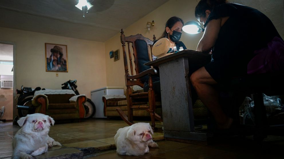 Marylin Alvarez, right, prepares a client's nails in the salon at her home as her two dogs lounge on the floor, at the Bahía neighborhood of Havana, Cuba, Wednesday, May 18, 2022. During President Barack Obama's administration, Alvarez began transfor