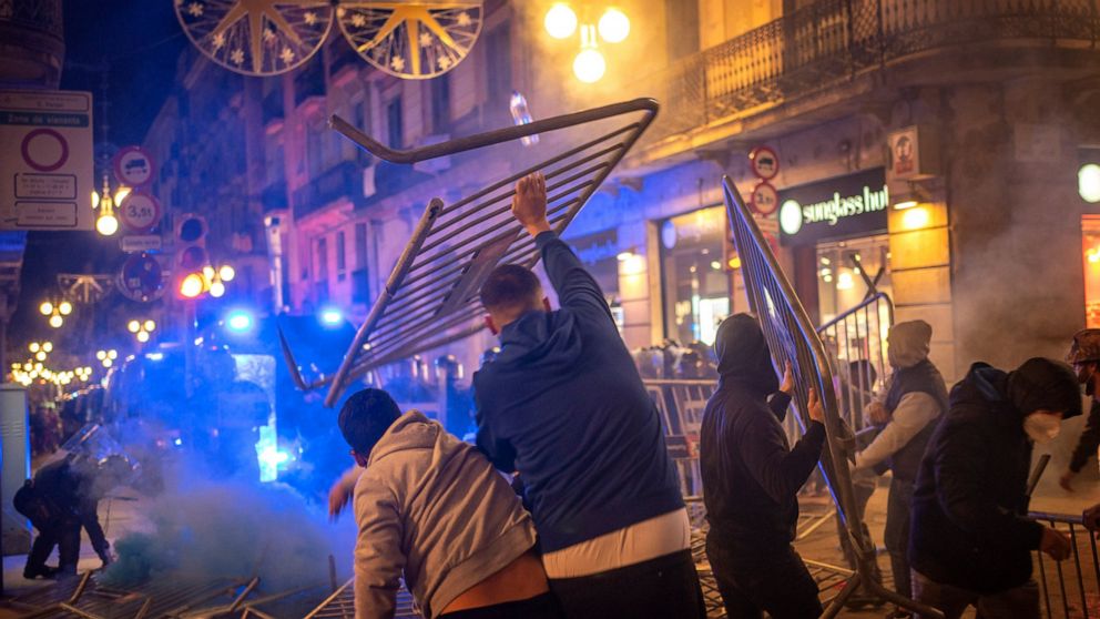 Demonstrators throw metallic fences against police during clashes in downtown Barcelona, Spain, Friday, Oct. 30, 2020. Clashes have erupted in a central Barcelona square between anti-riot police and hundreds who had gathered to protest the mandatory 