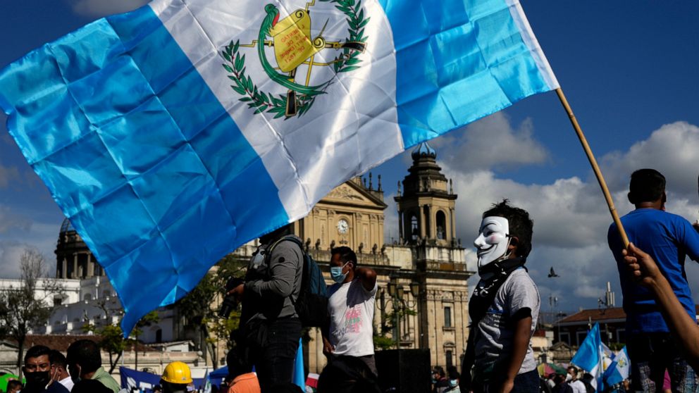 A child wearing a Guy Fawkes' mask often linked to popular movements stands on a stage during a rally to pressure Guatemalan President Alejandro Giammattei to resign, in Guatemala City, Saturday, July 31, 2021. The protest comes in response to the fi
