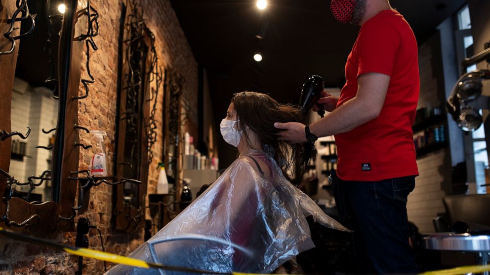 A woman, wearing a mask to protect against the spread of coronavirus, gets her hair styled in a hairdresser shop in downtown Brussels, Monday, July 27, 2020. Belgian Prime Minister Sophie Wilmes unveiled Monday a new set of drastic social distancing 